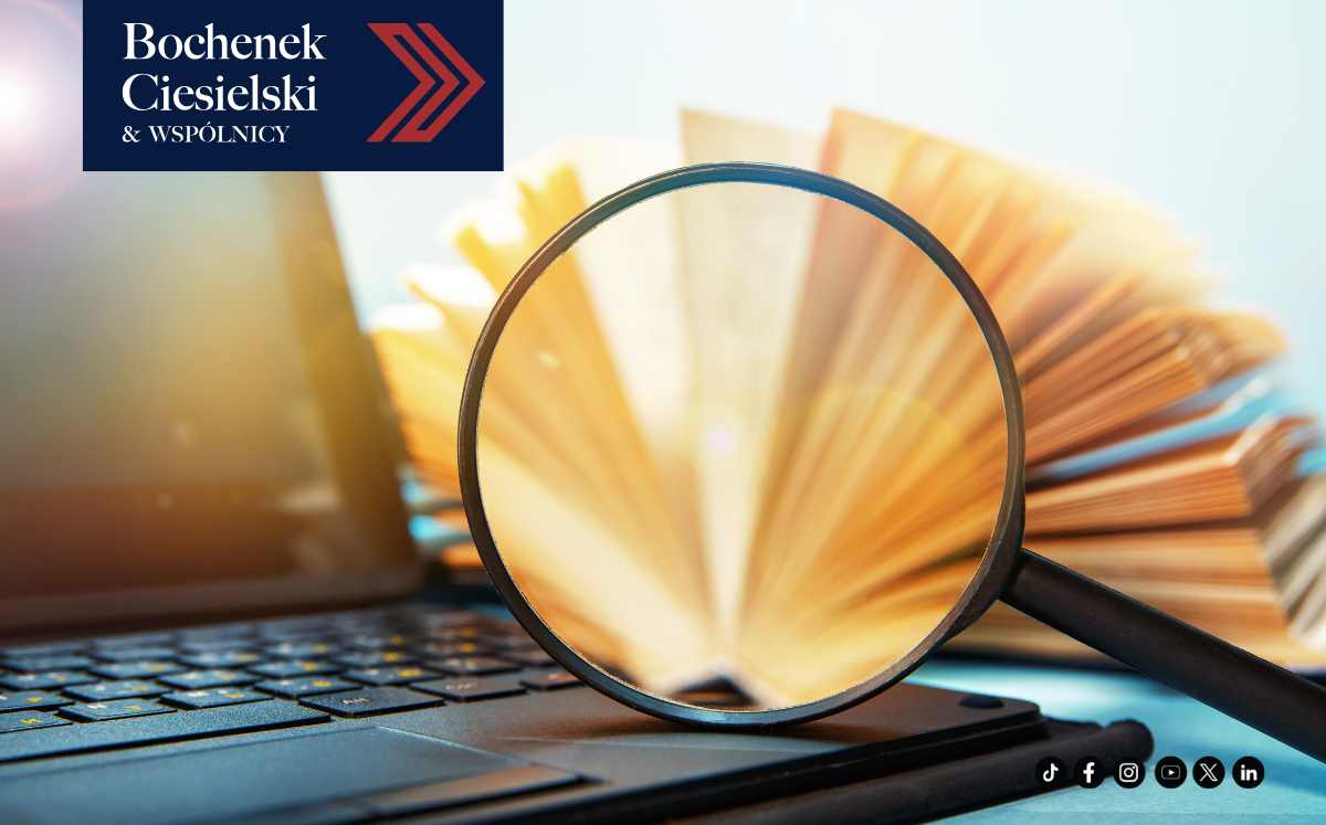 Szkło powiększające nad klawiaturą laptopa, w tle otwarta książka – wizualizacja analizy prawnej w kancelarii Bochenek Ciesielski & Wspólnicy.