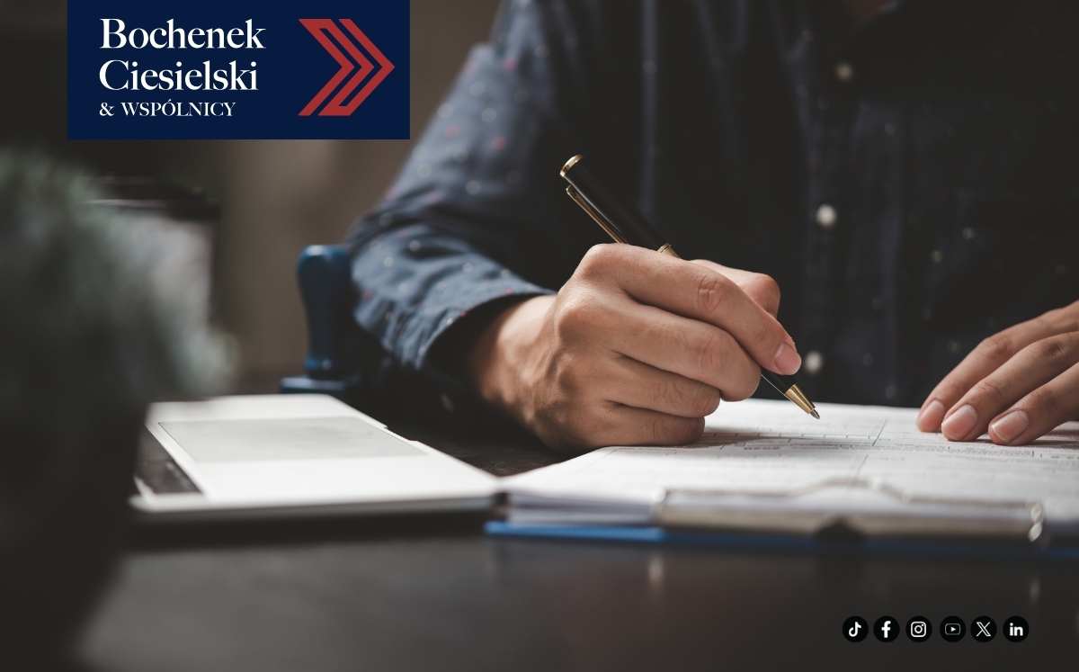 Mężczyzna piszący w notatniku przy biurku, obok tablet, w lewym górnym rogu logo Bochenek Ciesielski & Wspólnicy.