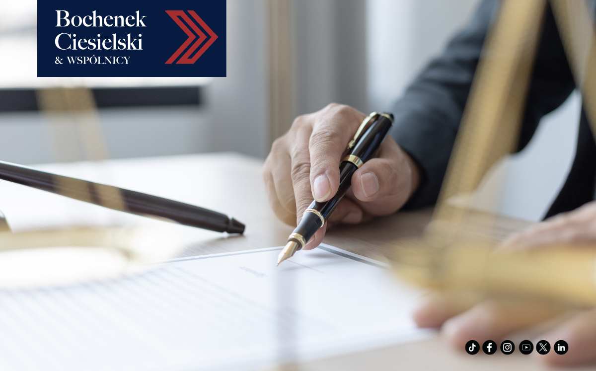 Zbliżenie na rękę mężczyzny podpisującego dokument eleganckim piórem, w tle niewyraźne elementy sali sądowej, w lewym górnym rogu logo kancelarii Bochenek Ciesielski & Wspólnicy.
