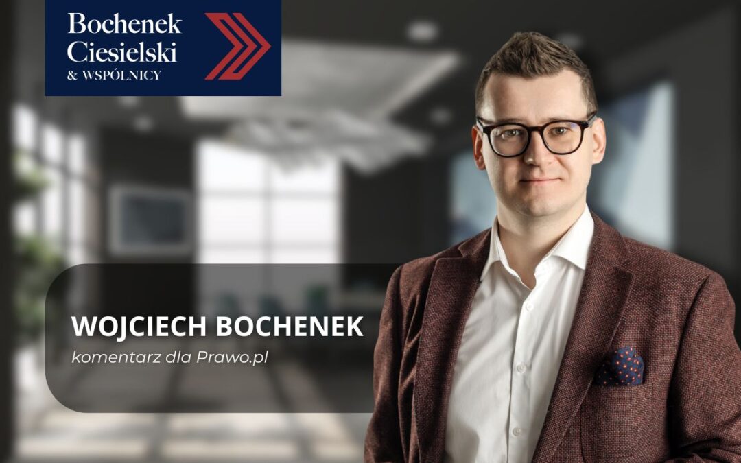 Prawnik Wojciech Bochenek w okularach i marynarce stoi w nowoczesnym biurze. Na zdjęciu widoczne logo kancelarii Bochenek Ciesielski & Wspólnicy oraz podpis: Wojciech Bochenek – komentarz dla Prawo.pl.