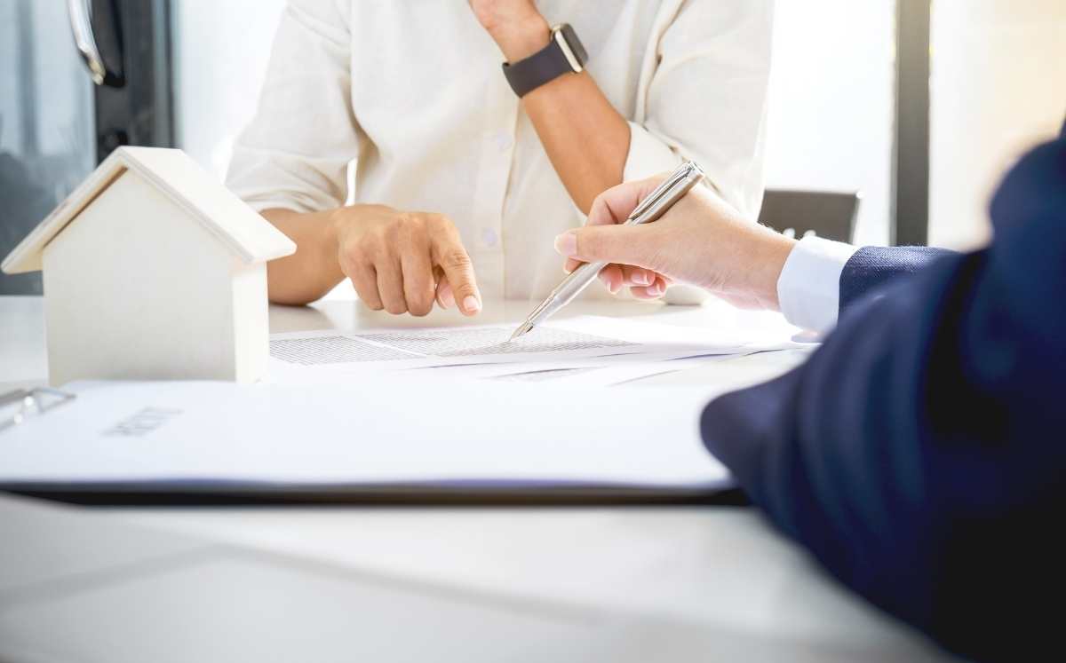 Dwie osoby omawiają dokumenty dotyczące kredytu hipotecznego, na biurku stoi model domu.