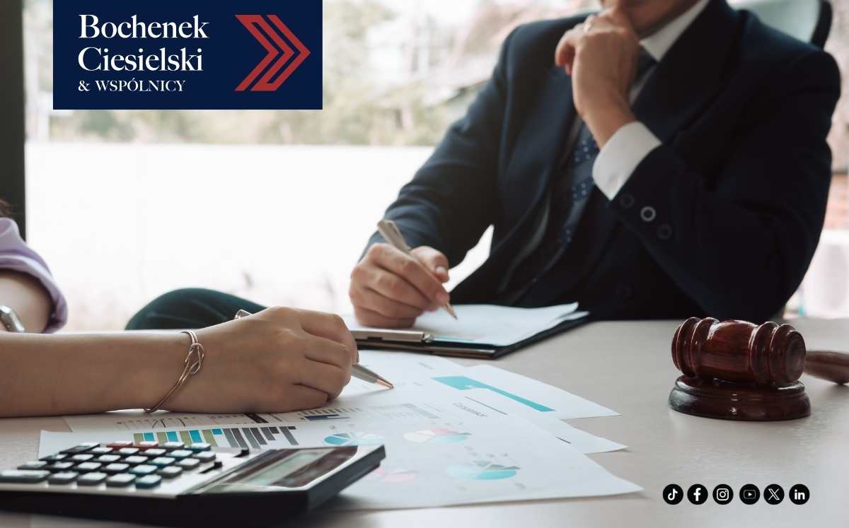 Dwoje prawników omawia dokumenty i wykresy przy biurku. Na stole leży młotek sędziowski i kalkulator. W lewym górnym rogu logo Bochenek Ciesielski & Wspólnicy.