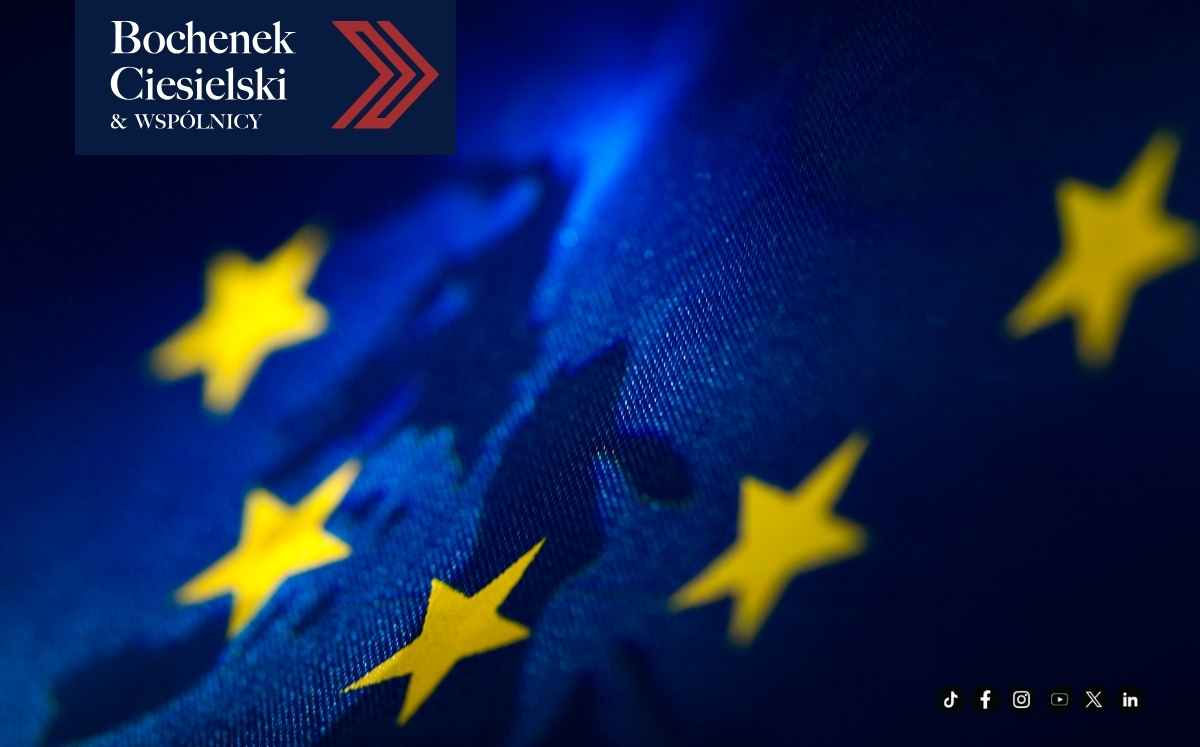 Zbliżenie na falującą flagę Unii Europejskiej na granatowym tle z żółtymi gwiazdami oraz logo kancelarii Bochenek Ciesielski & Wspólnicy.