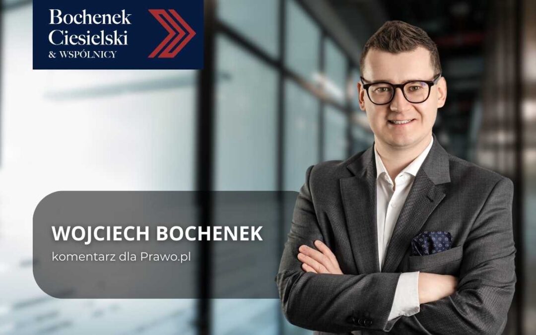 Mężczyzna w garniturze pozuje z rękami skrzyżowanymi na tle biura, obok widoczne logo kancelarii Bochenek Ciesielski & Wspólnicy oraz podpis komentarza prasowego.