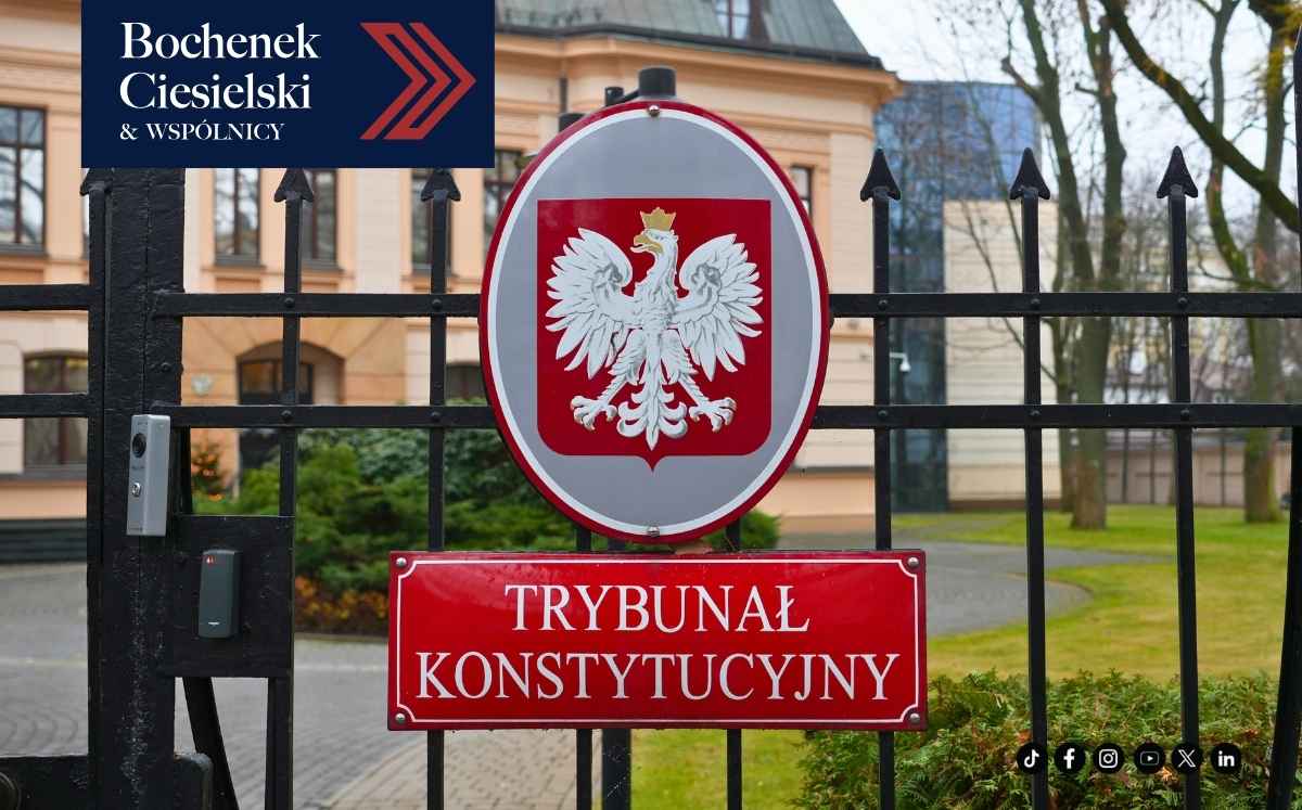 Wejście do budynku z ogrodzeniem, na którym umieszczony jest herb Polski oraz tablica z napisem ‘Trybunał Konstytucyjny’. W lewym górnym rogu widoczny jest logotyp Bochenek Ciesielski & Wspólnicy, a w prawym dolnym rogu ikony mediów społecznościowych.