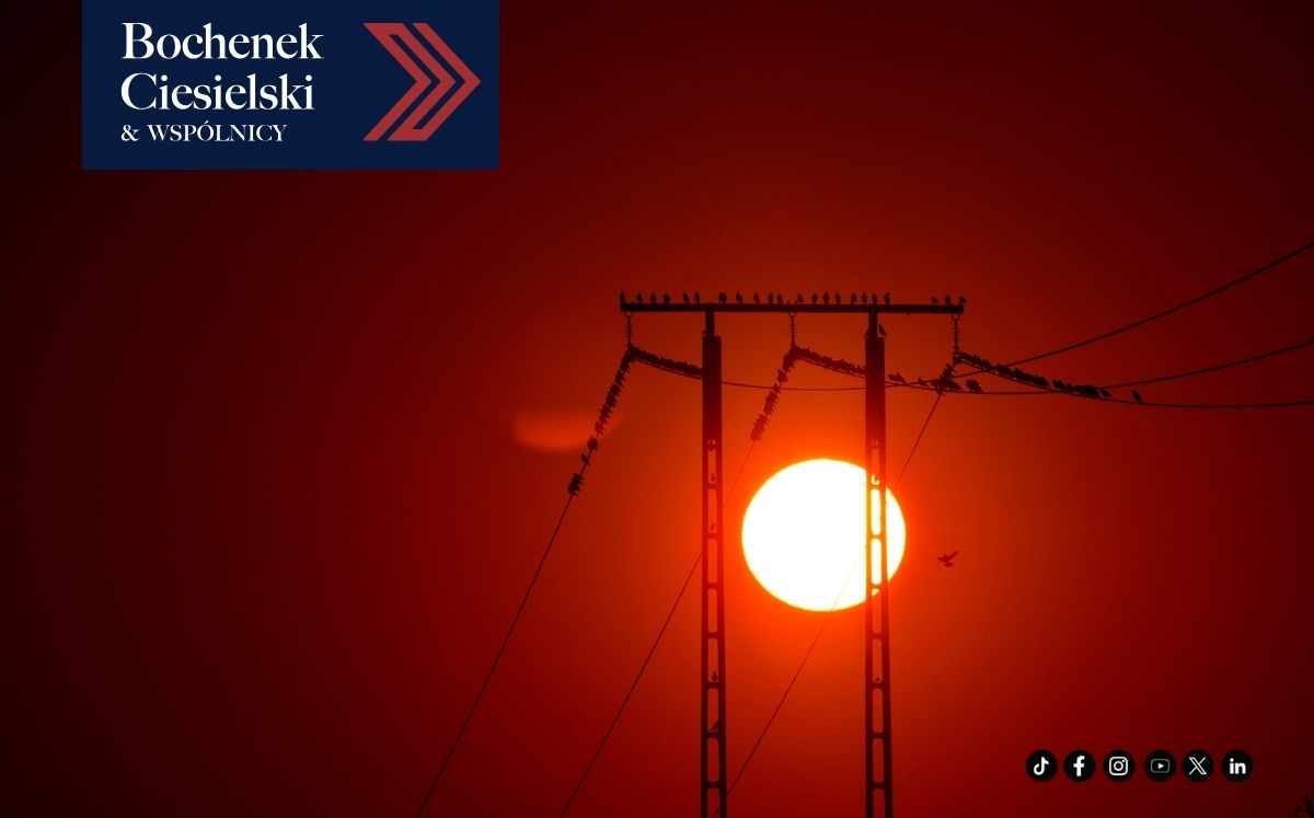Linie energetyczne na tle intensywnego zachodu słońca z ptakami siedzącymi na przewodach, w lewym górnym rogu logo kancelarii Bochenek Ciesielski & Wspólnicy.