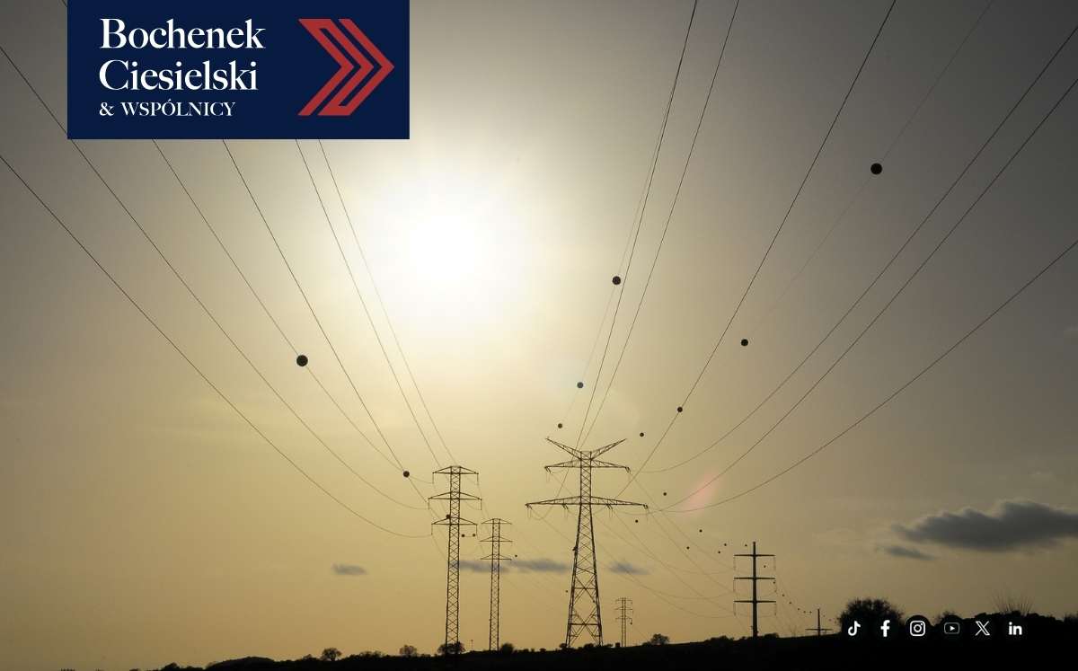 Słupy i przewody energetyczne pod jasnym niebem, ilustracja artykułu o służebności przesyłu z logo Bochenek Ciesielski & Wspólnicy.