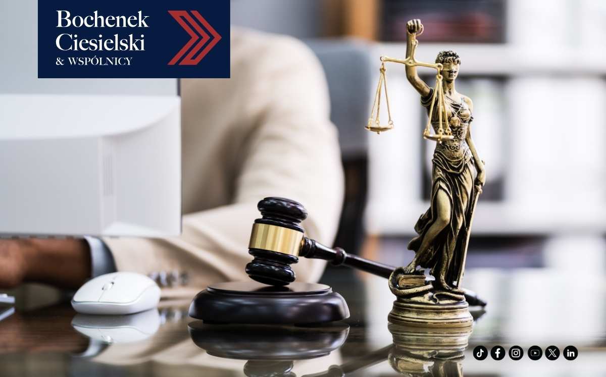 Figura Temidy oraz młotek sędziowski stojące na biurku; w tle osoba pracująca przy komputerze. W lewym górnym rogu widoczne logo Bochenek Ciesielski & Wspólnicy.
