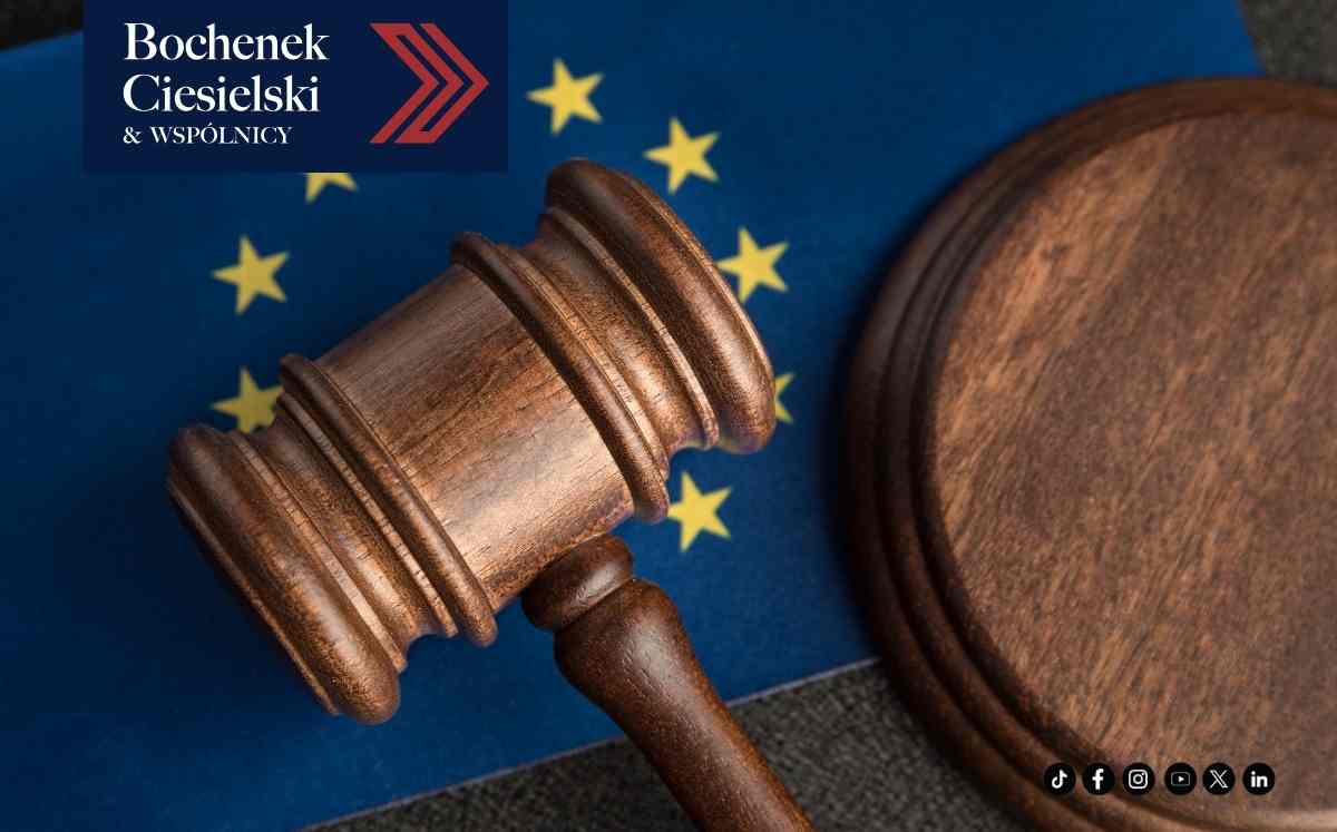 Drewniany młotek sędziowski leżący na tle flagi Unii Europejskiej, symbol orzecznictwa TSUE i prawa europejskiego, z logo Bochenek Ciesielski & Wspólnicy.