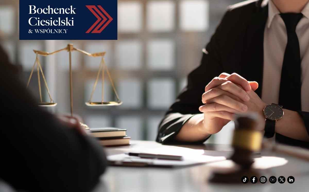 Prawnik siedzący przy biurku z wagą sprawiedliwości i dokumentami podczas konsultacji prawnej.