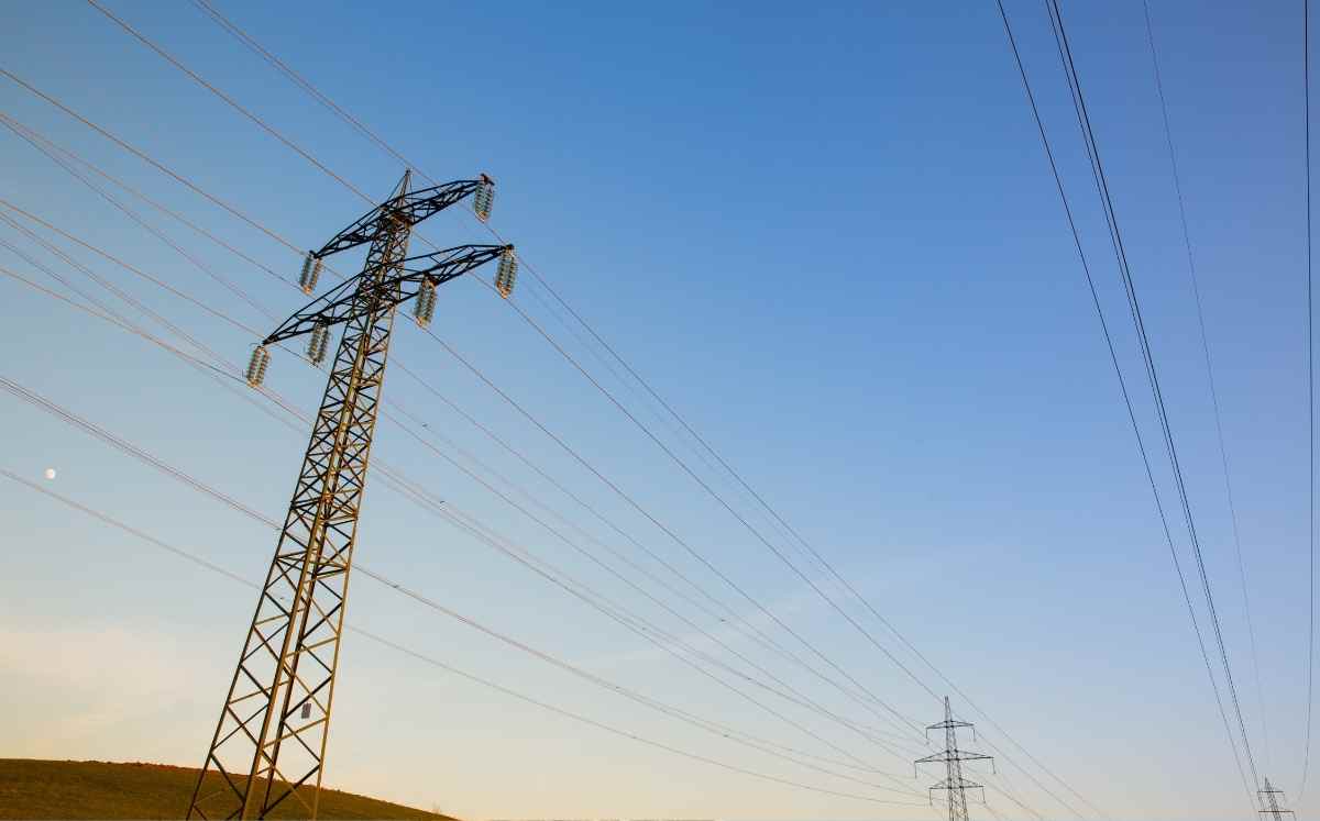 Linia elektroenergetyczna z wysokimi słupami przesyłowymi na tle czystego, błękitnego nieba.