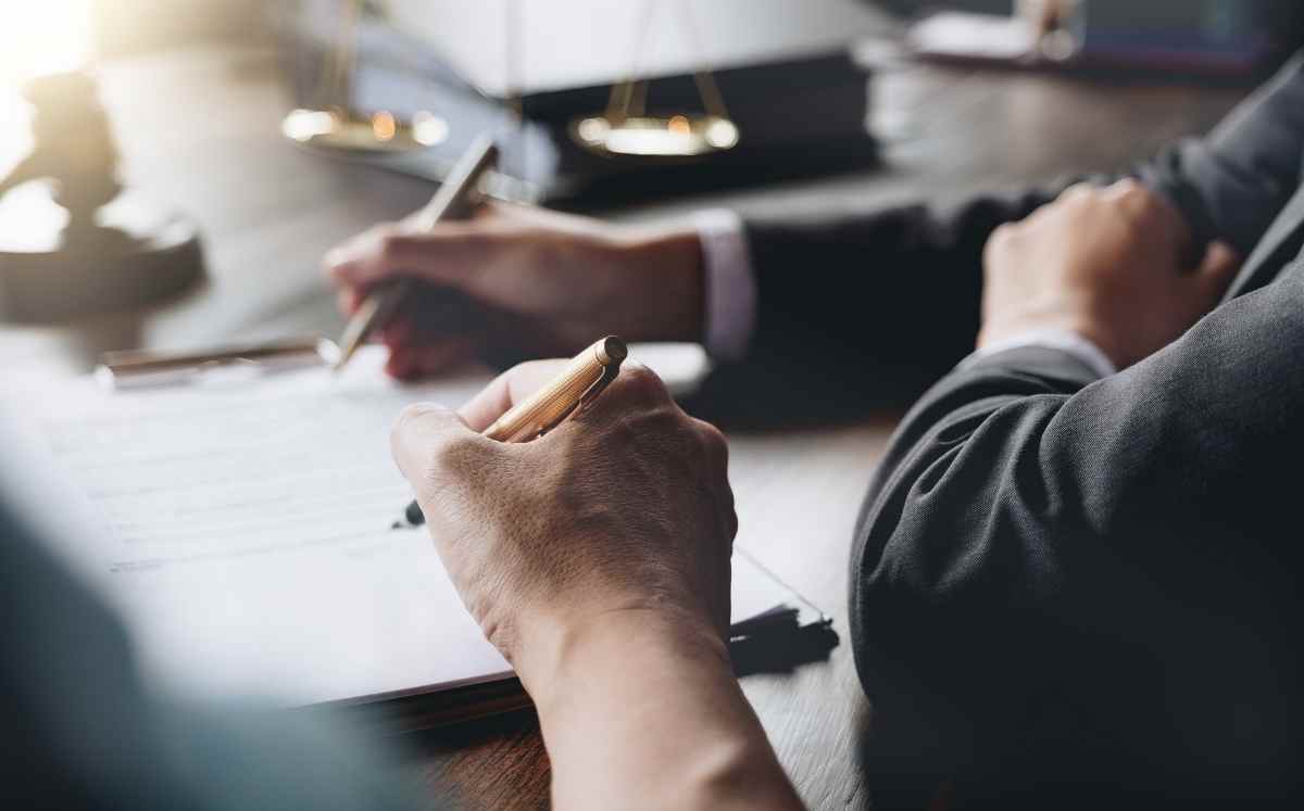 Dwie osoby w formalnych strojach podpisują dokument przy stole podczas spotkania prawnego.