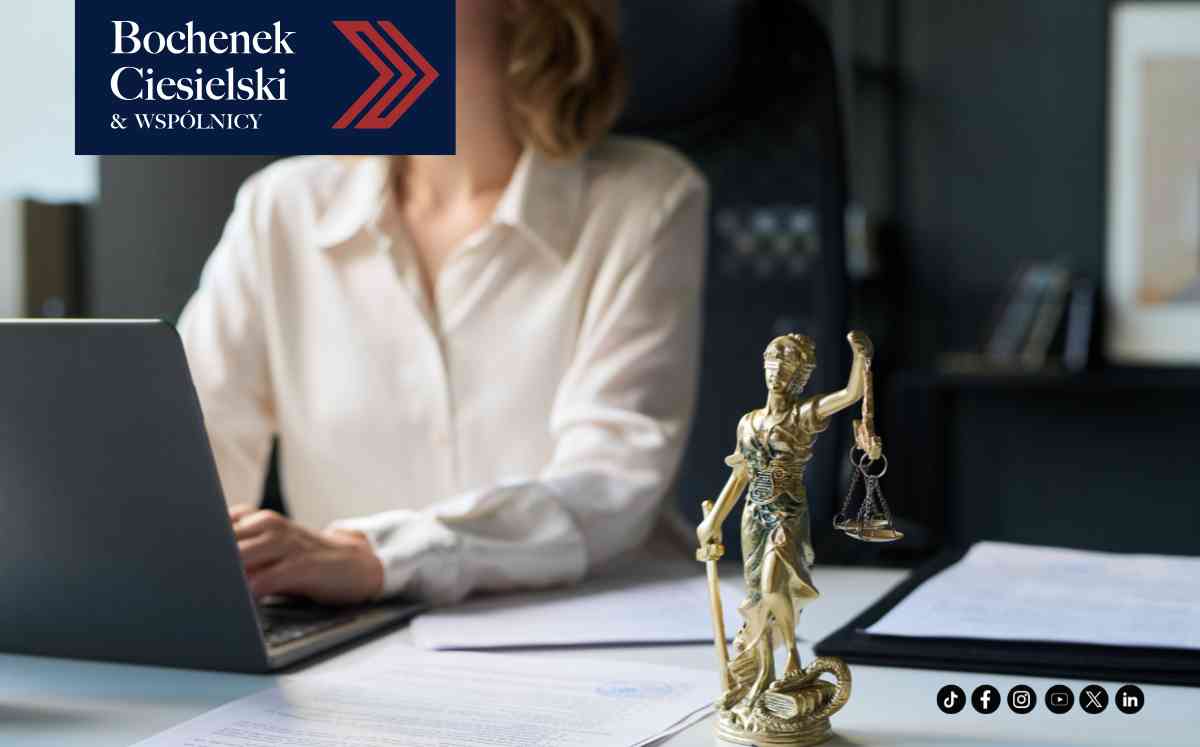 Statua Temidy trzymająca wagę na biurku kancelarii obok prawnika analizującego dokumenty na laptopie.