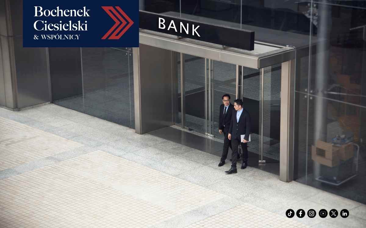 Dwóch mężczyzn wychodzi z nowoczesnego budynku banku. W lewym górnym rogu widoczne logo kancelarii Bochenek, Ciesielski i Wspólnicy.