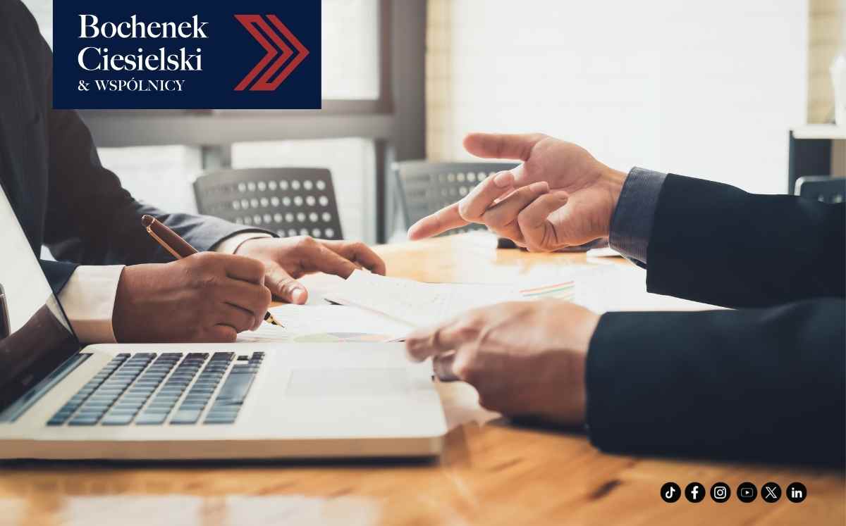 Dwóch mężczyzn podpisujących dokument przy biurku z laptopem – spotkanie biznesowe lub konsultacja prawna.