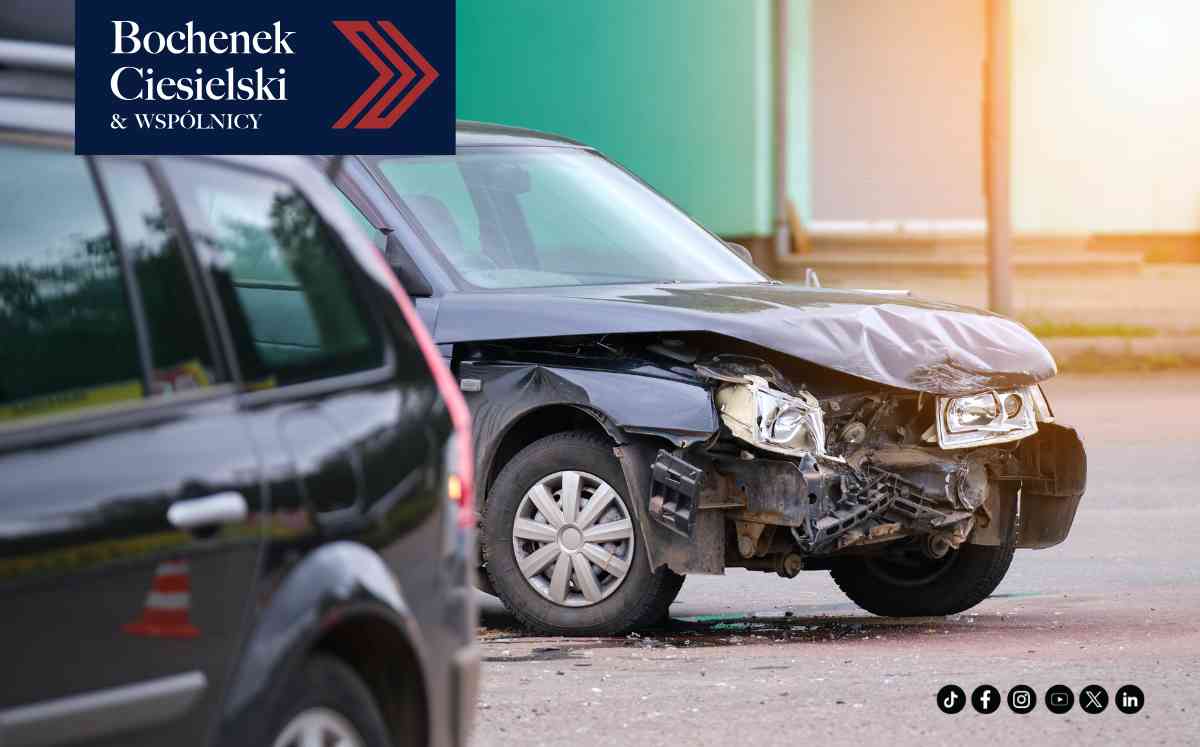 Mocno uszkodzony przód czarnego samochodu po wypadku drogowym, ze zniszczoną maską i reflektorem.