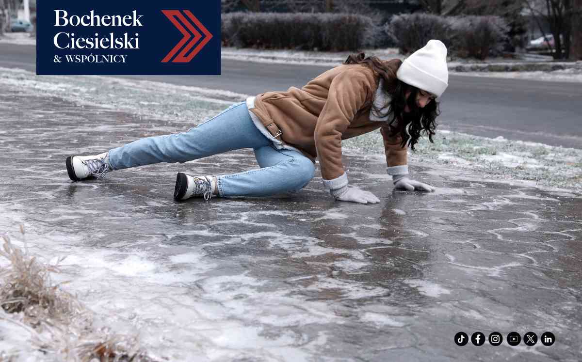 Kobieta upadająca na oblodzonym chodniku w zimowy dzień, podpierająca się rękami o lód