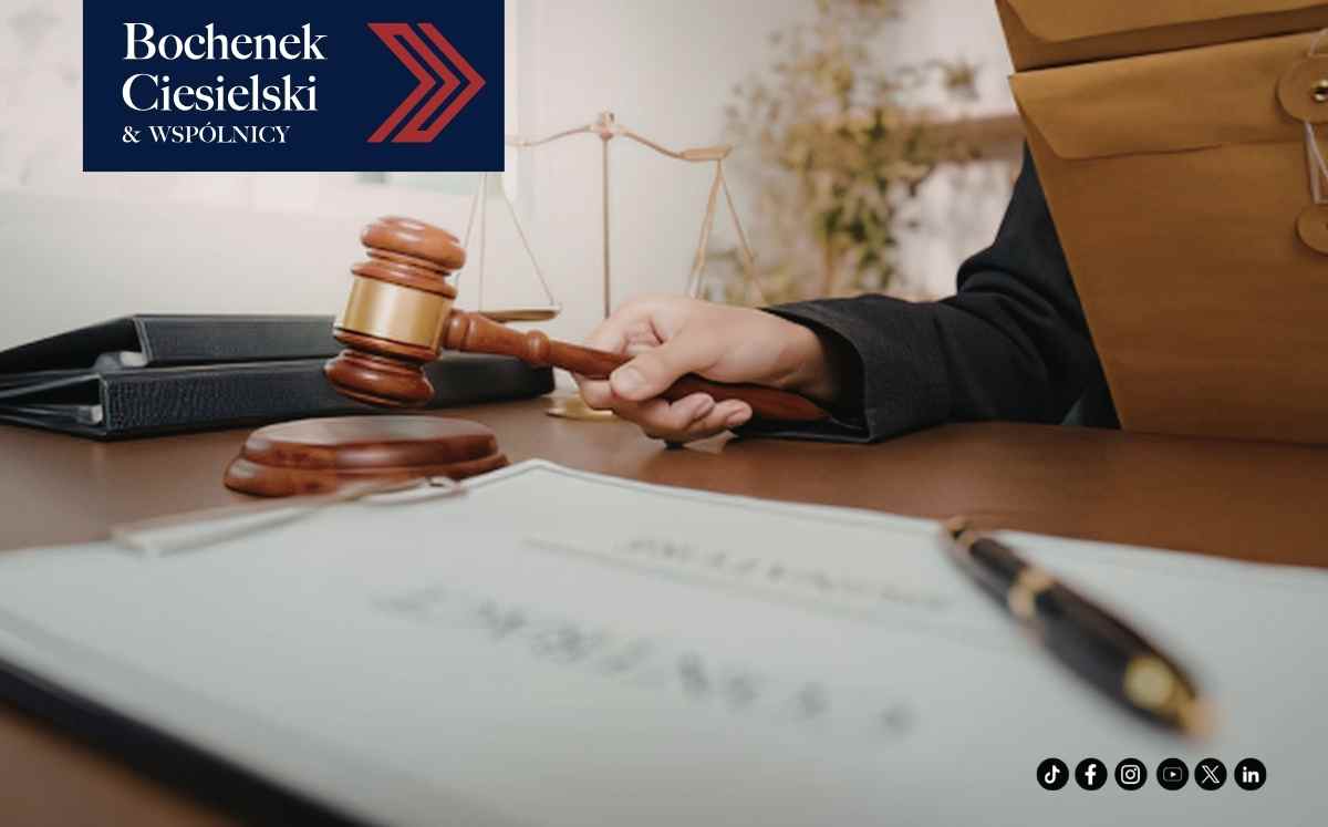 Dłoń trzymająca młotek sędziowski nad biurkiem, w tle waga sprawiedliwości i logo kancelarii Bochenek, Ciesielski i Wspólnicy.