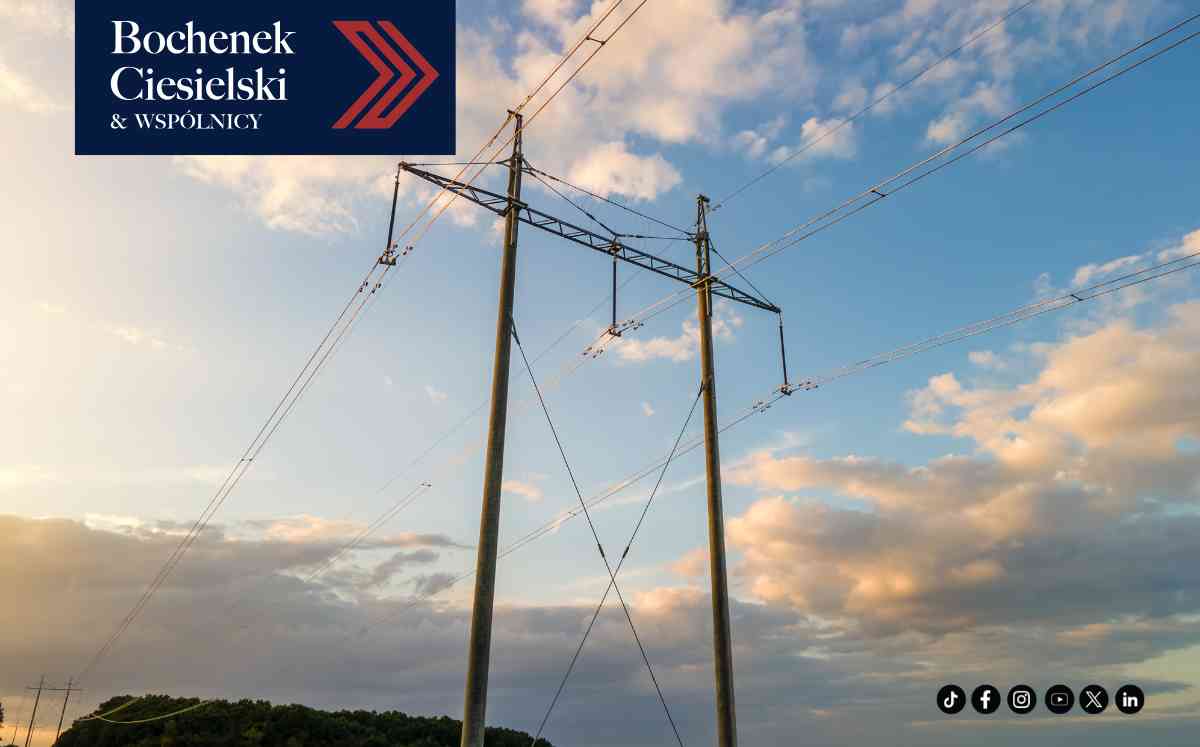 Zbliżenie na stalowy słup elektroenergetyczny z licznymi przewodami na tle błękitnego nieba z jasnymi chmurami.