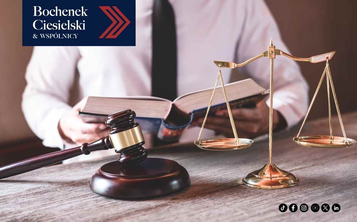 Młotek sędziowski, waga sprawiedliwości i otwarta księga prawa na biurku, w tle prawnik; grafika kancelarii Bochenek Ciesielski & Wspólnicy.