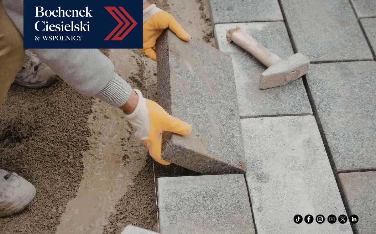 Pracownik układa kostkę brukową na podsypce, obok leży gumowy młotek.