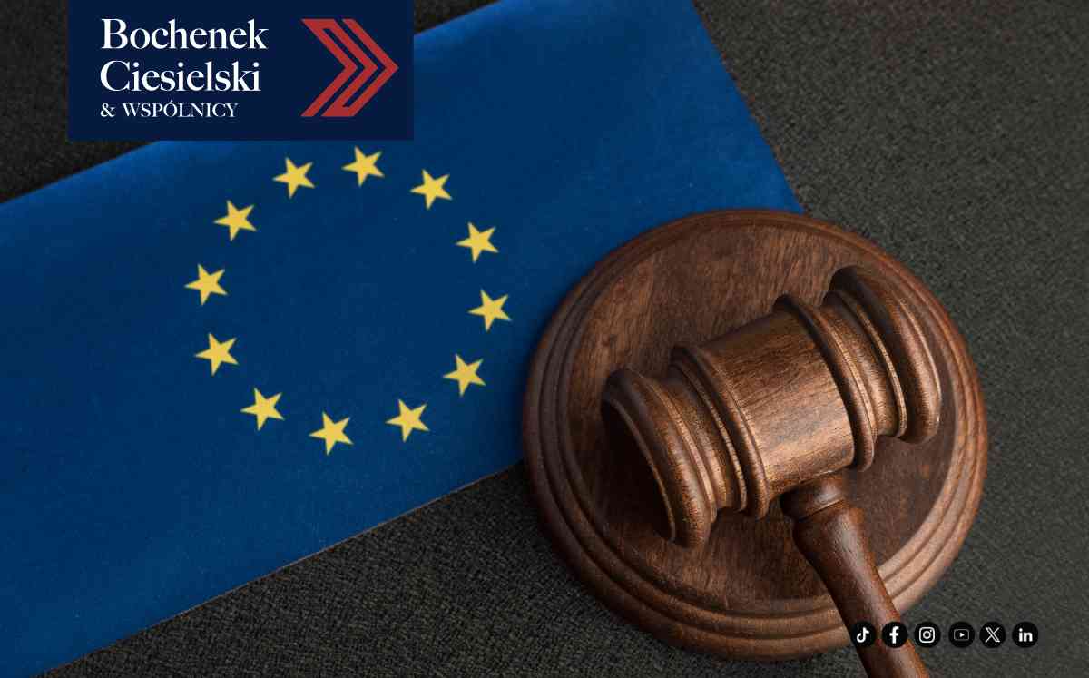 Wooden gavel resting on a dark surface beside the European Union flag and law-firm branding in the corner