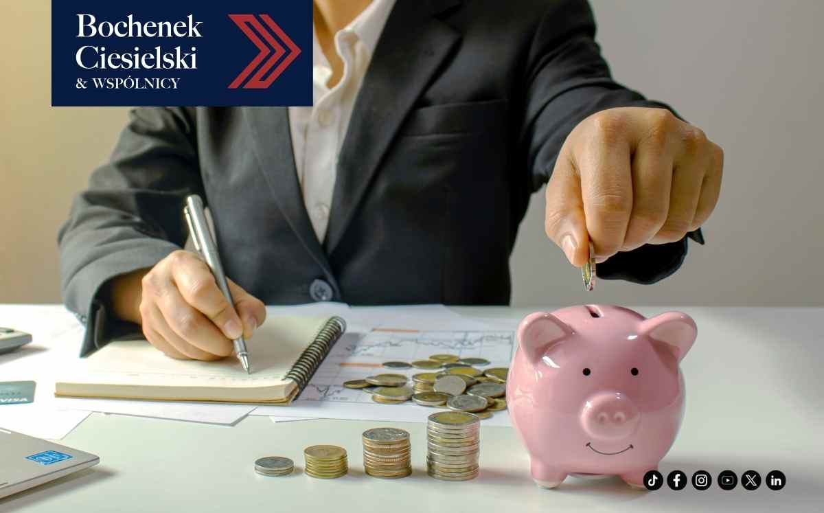 Businessperson in a suit saves money at a desk with a pink piggy bank, coins, and documents; firm logo Bochenek Ciesielski & Wspólnicy in the corner.