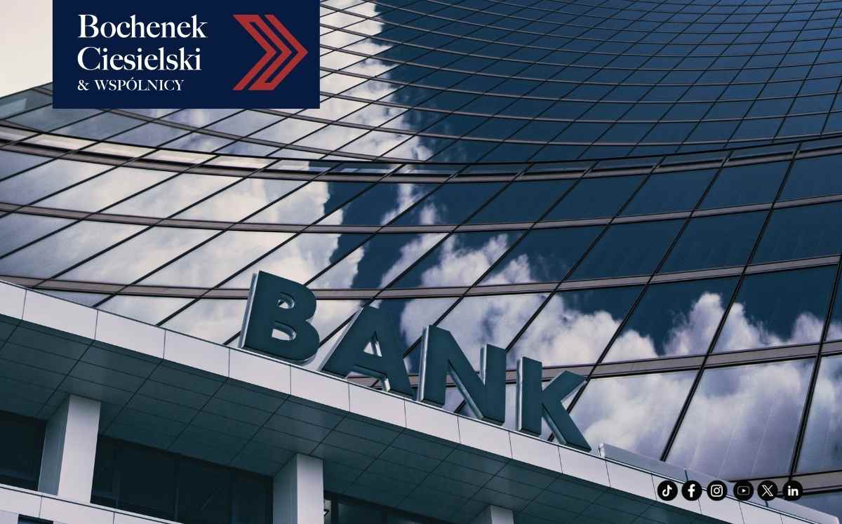 Glass-waced bank building with large 'BANK' sign and a blue logo panel reading 'Bochenek Ciesielski & Wspólnicy' in the corner, plus social icons at the bottom-right edge.