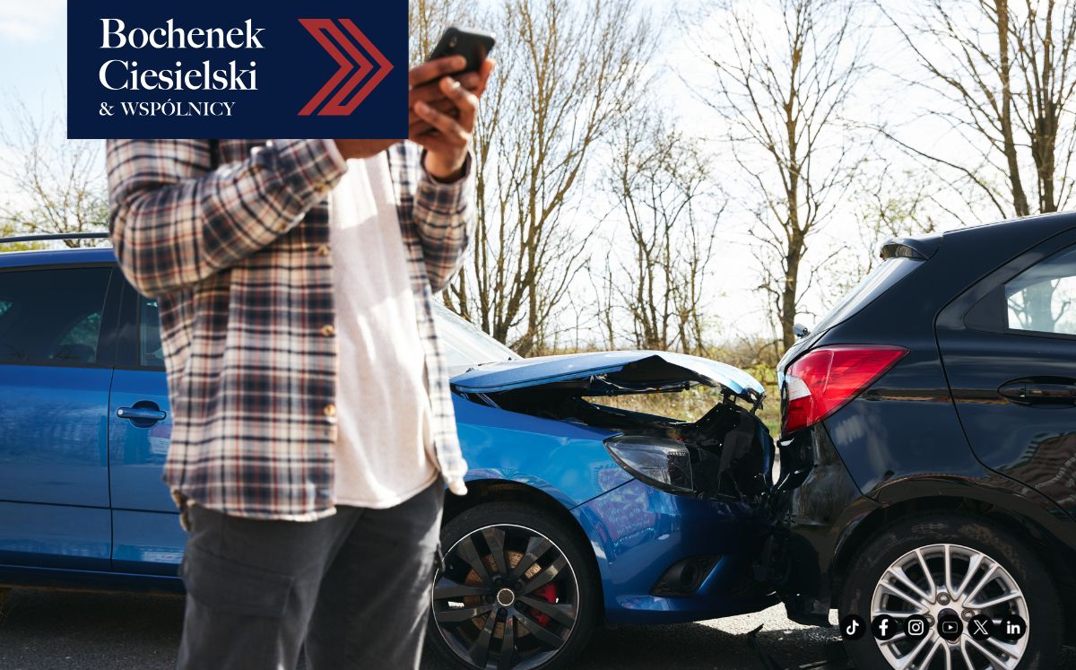 Osoba stojąca obok niebieskiego samochodu uszkodzonego w wyniku zderzenia tylnego z czarnym samochodem i patrząca na telefon; nakładka z logo w lewym górnym rogu.
