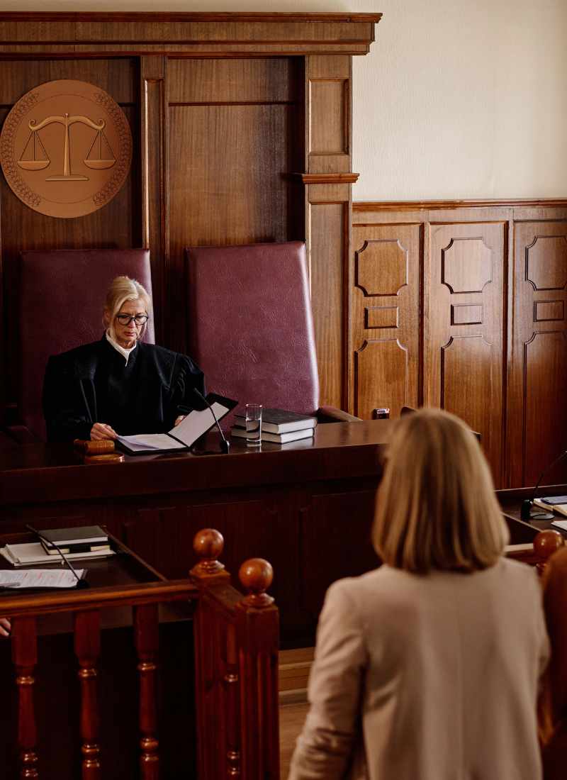Gavel about to strike a sound block on a courtroom desk with a judge in the background.