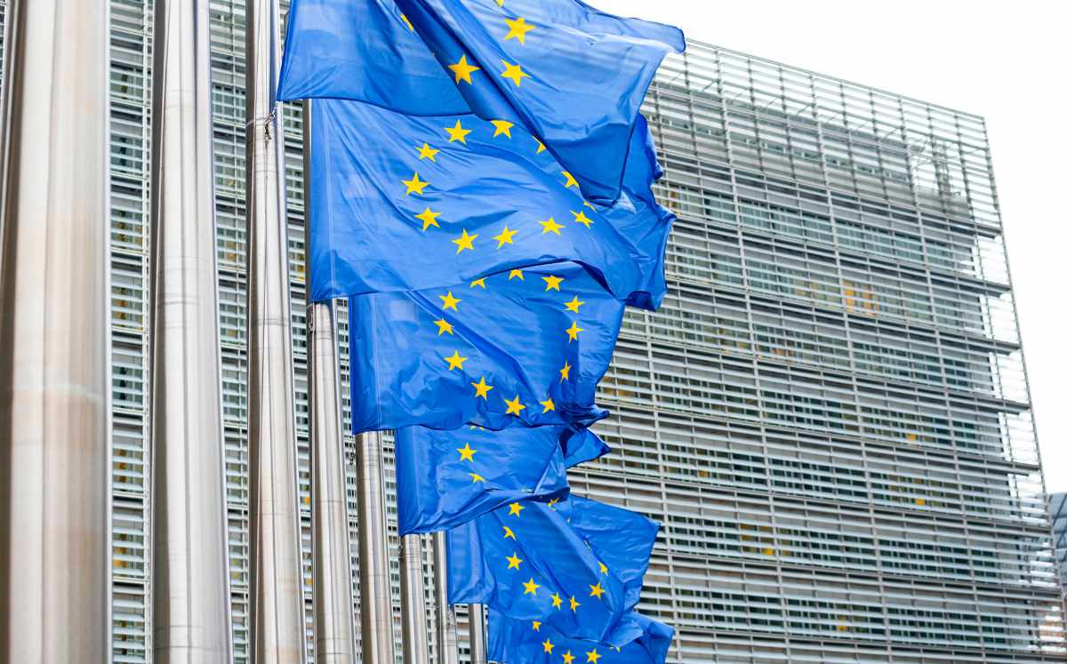 European Union flags waving outside a modern glass-and-metal government building.