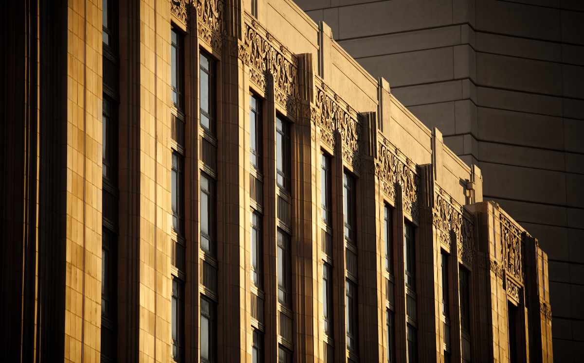 Sunlit beige stone facade with tall windows and ornate decorative reliefs along the top.
