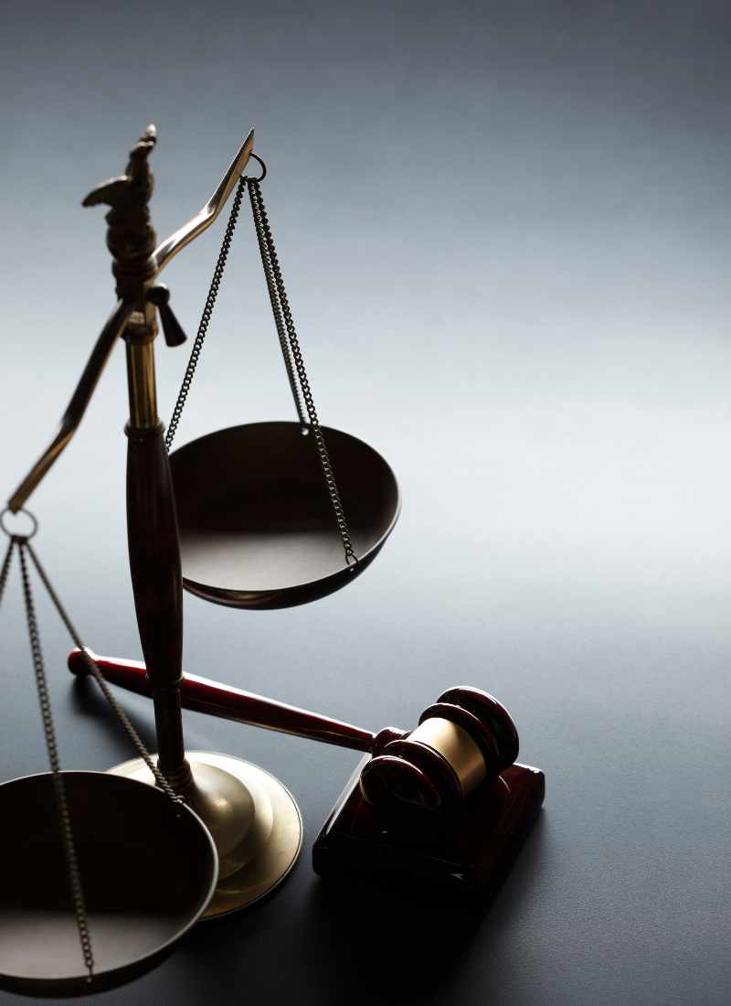 Balance scales of justice with a wooden gavel on a dark surface, symbolizing the legal system.