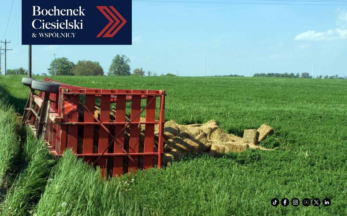 Zielone pole, na którym leży przewrócona czerwona przyczepa z sianem