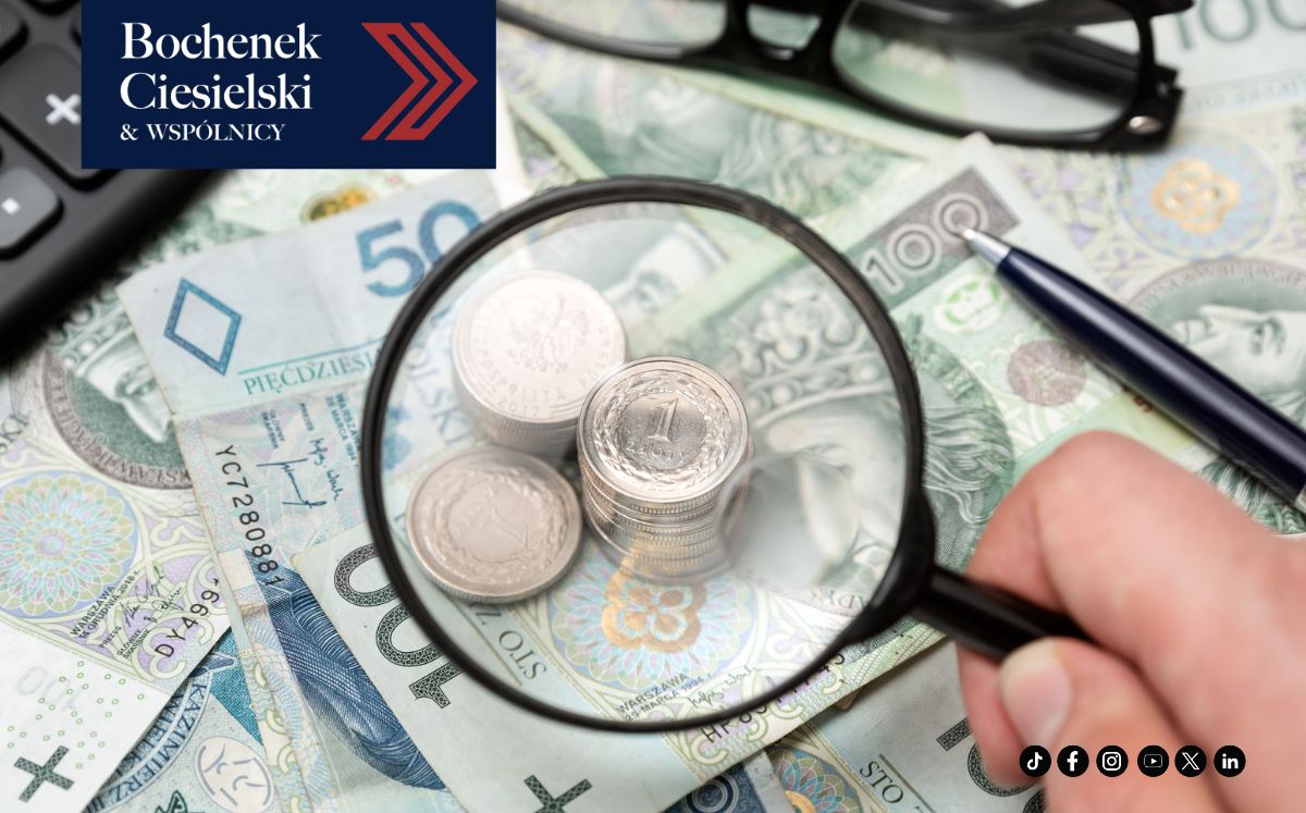 Lupa powiększająca monety leżące na banknotach w otoczeniu rekwizytów biurowych